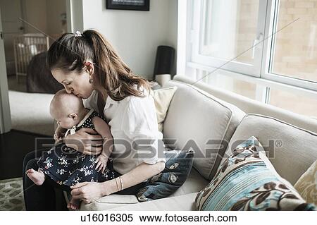 Stock Photography - Mother kissing baby daughter's (2-5 months) head in living room. Fotosearch