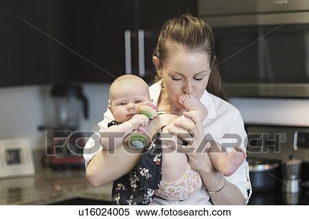 Stock Photography - Mother kissing baby daughter's (2-5 months) feet. Fotosearch