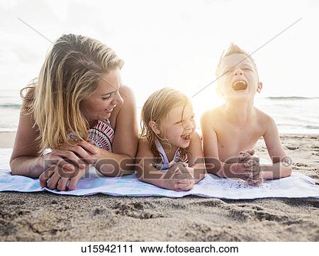 Stock Image - Mother lying down with son (6-7) and daughter (4-5) on beach. Fotosearch