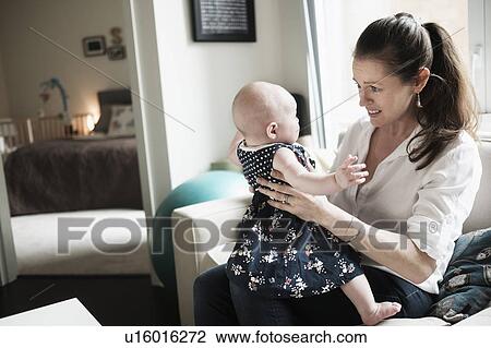 Stock Image - Mother playing with baby daughter (2-5 months) in living room. Fotosearch