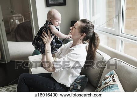 Stock Image - Mother playing with baby daughter (2-5 months) in living room. Fotosearch