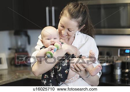 Stock Image - Mother playing with baby daughter (2-5 months) in kitchen. Fotosearch