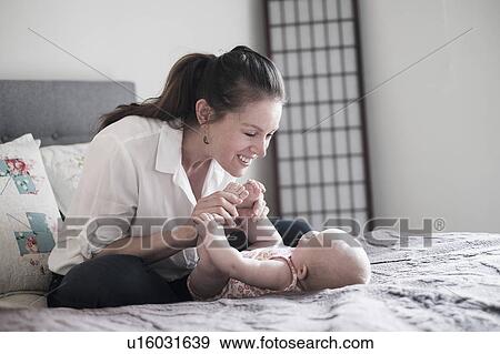 Stock Photo - Mother playing with baby daughter (2-5 months) in bedroom. Fotosearch