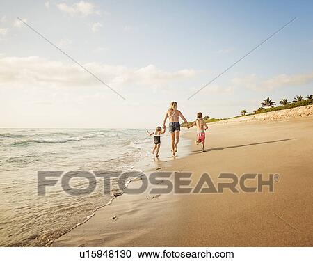 Mother running with boy (6-7) and girl (4-5) on beach by water View Large Photo Image Stock Image - Mother running with boy (6-7) and girl (4-5) on beach by water. Fotosearch