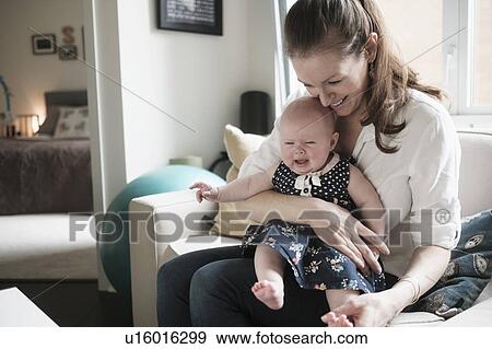 Mother sitting on sofa with crying baby daughter (2-5 months) in living room View Large Photo Image Stock Photo - Mother sitting on sofa with crying baby daughter (2-5 months) in living room. Fotosearch