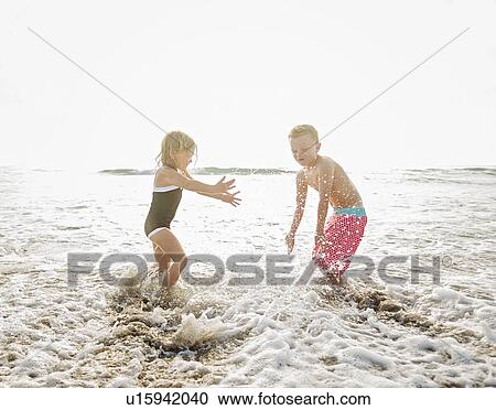 Stock Image - Mother walking with boy (6-7) and girl (4-5) on beach by water. Fotosearch