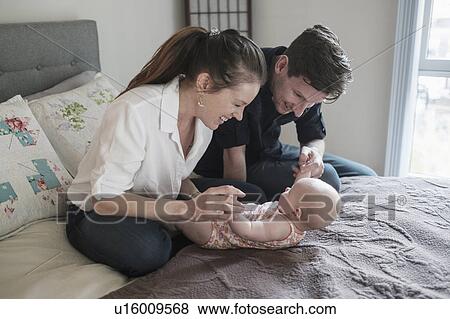 Parents playing with baby daughter (2-5 months) in bedroom View Large Photo Image Stock Photo - Parents playing with baby daughter (2-5 months) in bedroom. Fotosearch