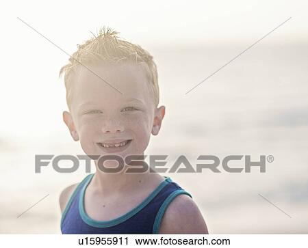 Stock Image - Portrait of boy (6-7) in blue tank top at beach. Fotosearch