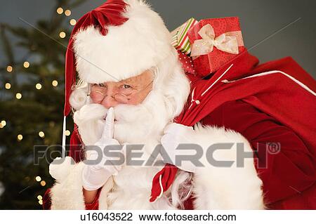 Stock Image - Portrait of Santa Claus with finger on lips, carrying sack over shoulder. Fotosearch