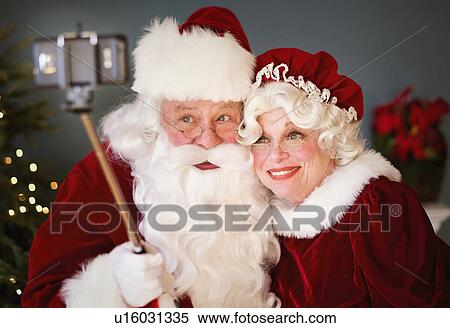 Stock Photography - Santa and Mrs. Santa taking selfie with monopod. Fotosearch
