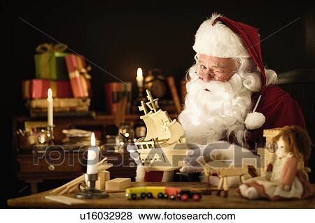 Stock Photo - Santa Claus making wooden toy and winking. Fotosearch