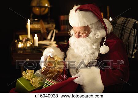 Stock Photo - Santa Claus packing Christmas presents to sack. Fotosearch