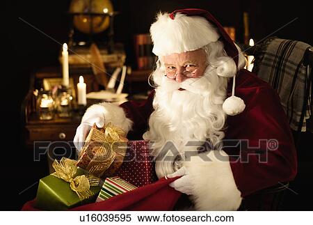 Stock Photography - Santa Claus packing Christmas presents to sack. Fotosearch