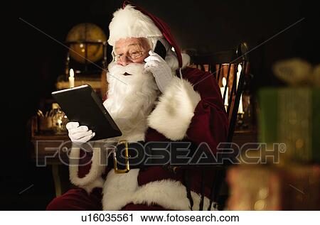 Stock Image - Santa Claus using digital tablet and talking by mobile phone. Fotosearch