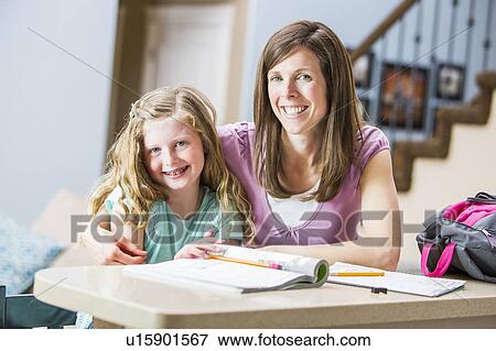 Stock Photo - Smiling mother and daughter (8-9) sitting at table studying. Fotosearch