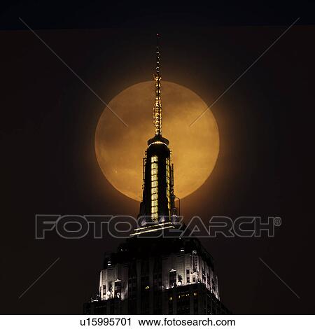 Stock Image - Spire of Empire State Building with full moon in background. Fotosearch