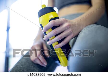 Stock Photo - Woman holding water bottle in gym. Fotosearch