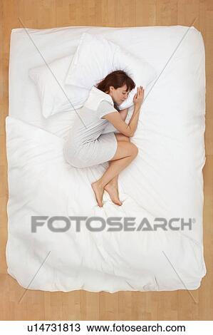 Stock Image - Woman lying in bed, asleep. Fotosearch