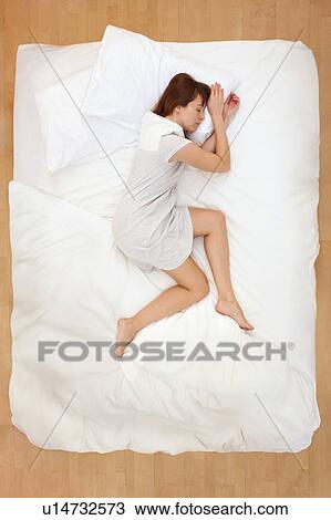 Stock Image - Woman lying in bed, asleep. Fotosearch