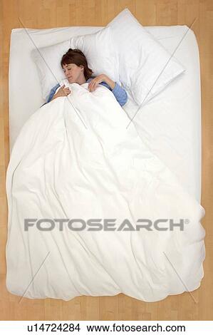 Picture - Woman lying in bed holding duvet. Fotosearch