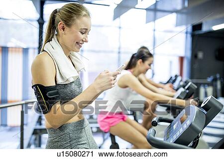 Stock Image - Woman using phone in gym. Fotosearch