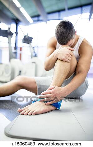 Stock Photo - Young man holding ice pack on ankle. Fotosearch