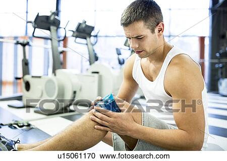 Stock Image - Young man holding ice pack on knee. Fotosearch