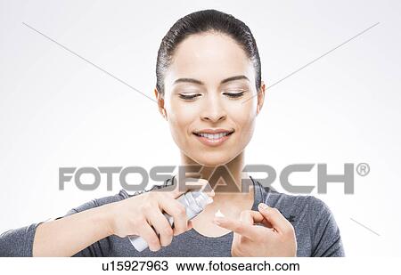 Stock Image - Young woman applying moisturizer. Fotosearch