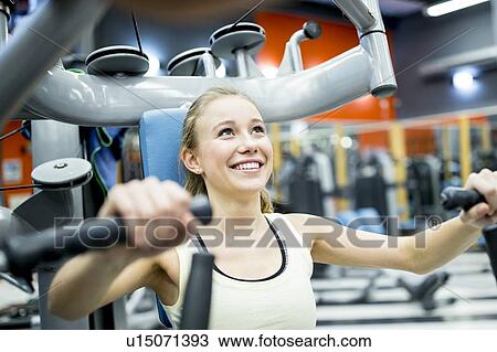 Stock Image - Young woman doing chest press. Fotosearch