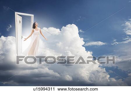 Stock Image - Young woman getting out from door in clouds. Fotosearch