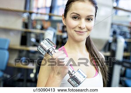 Stock Image - Young woman holding dumbbell. Fotosearch
