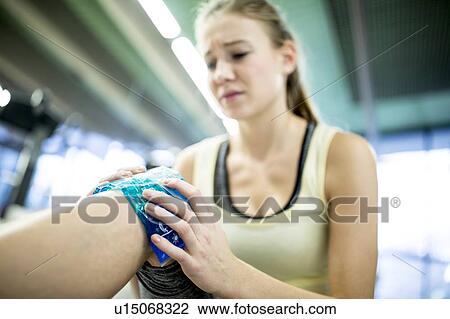 Stock Image - Young woman holding ice pack on knee. Fotosearch