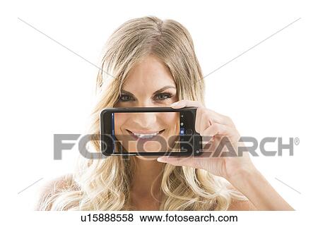 Young woman holding smart phone displaying smile against face View Large Photo Image Stock Photo - Young woman holding smart phone displaying smile against face. Fotosearch