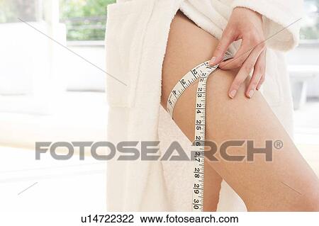 Stock Image - Young woman measuring thigh. Fotosearch