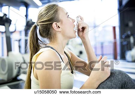 Stock Image - Young woman using inhaler. Fotosearch