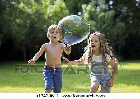Stock Image - Brother and sister chasing bubbles. Fotosearch