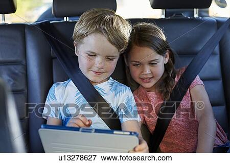 Stock Photo - Brother and sister in car using tablet. Fotosearch