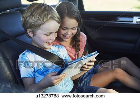 Stock Photo - Brother and sister in car using tablet. Fotosearch