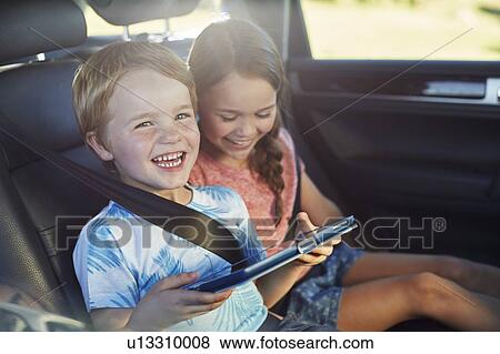 Stock Photo - Brother and sister in car using tablet. Fotosearch