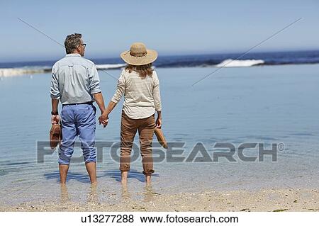 Stock Photo - Couple holding hands, paddling in the sea. Fotosearch