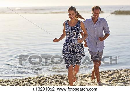 Stock Image - Couple running on to the beach. Fotosearch