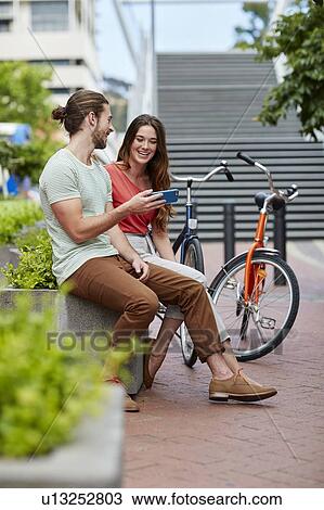 Couple sitting on wall with bikes View Large Photo Image Stock Image - Couple sitting on wall with bikes. Fotosearch