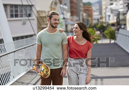 Picture - Couple walking, man carrying skateboard. Fotosearch