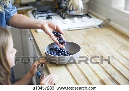 Stock Image - Girl looking at bowl of fresh blueberries. Fotosearch