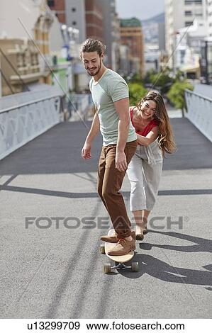 Man skateboarding with woman pushing View Large Photo Image Stock Photo - Man skateboarding with woman pushing. Fotosearch