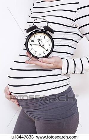 Stock Image - Pregnant woman holding alarm clock. Fotosearch