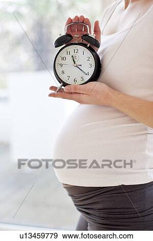 Pregnant woman holding alarm clock View Large Photo Image Stock Photo - Pregnant woman holding alarm clock. Fotosearch