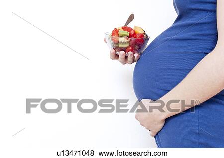 Stock Photo - Pregnant woman holding fruit salad. Fotosearch