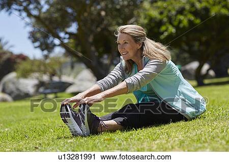 Stock Image - Senior woman stretching on grass. Fotosearch