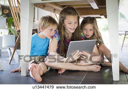 Three siblings under table with tablet View Large Photo Image Stock Photo - Three siblings under table with tablet. Fotosearch
